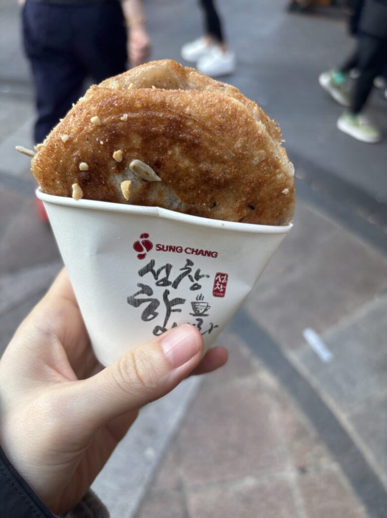 紙カップに入ったナッツ入りホットクを手に持っている写真